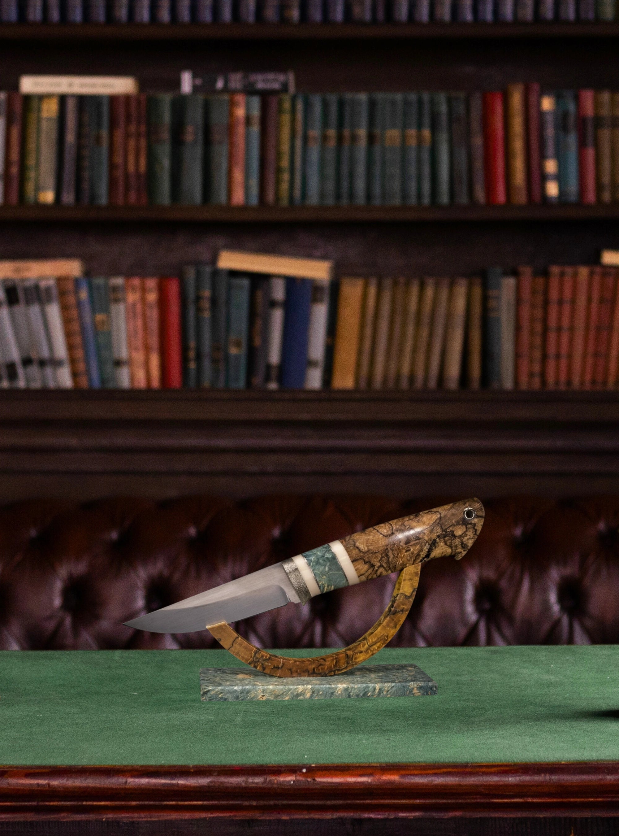 Decorative knife with decorative handle on a stand in front of a bookshelf.