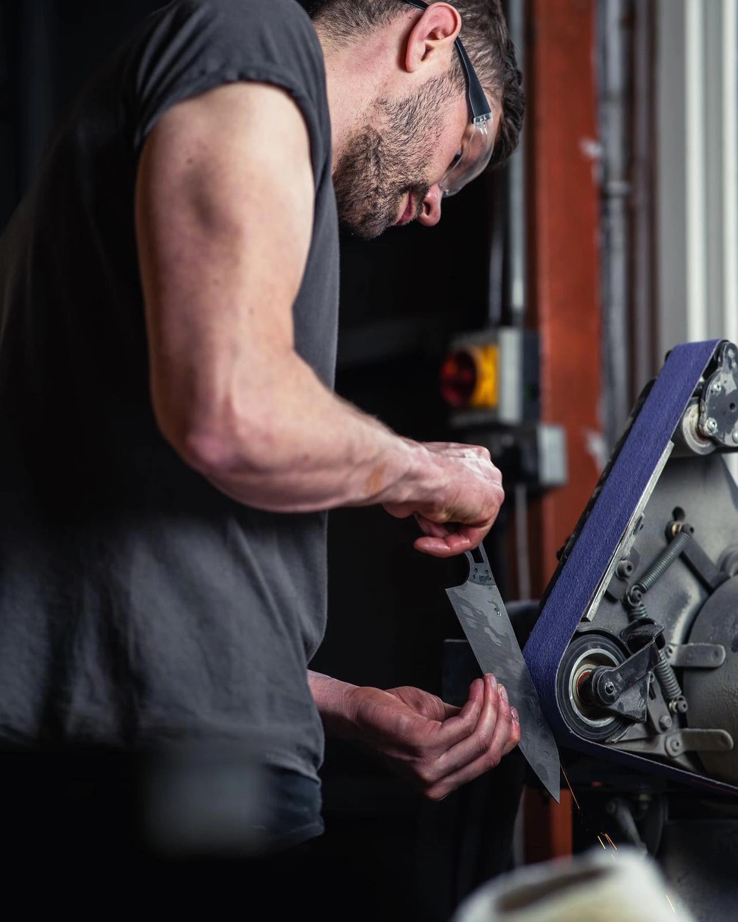 Man sharpening a knife using a belt sander in a workshop setting